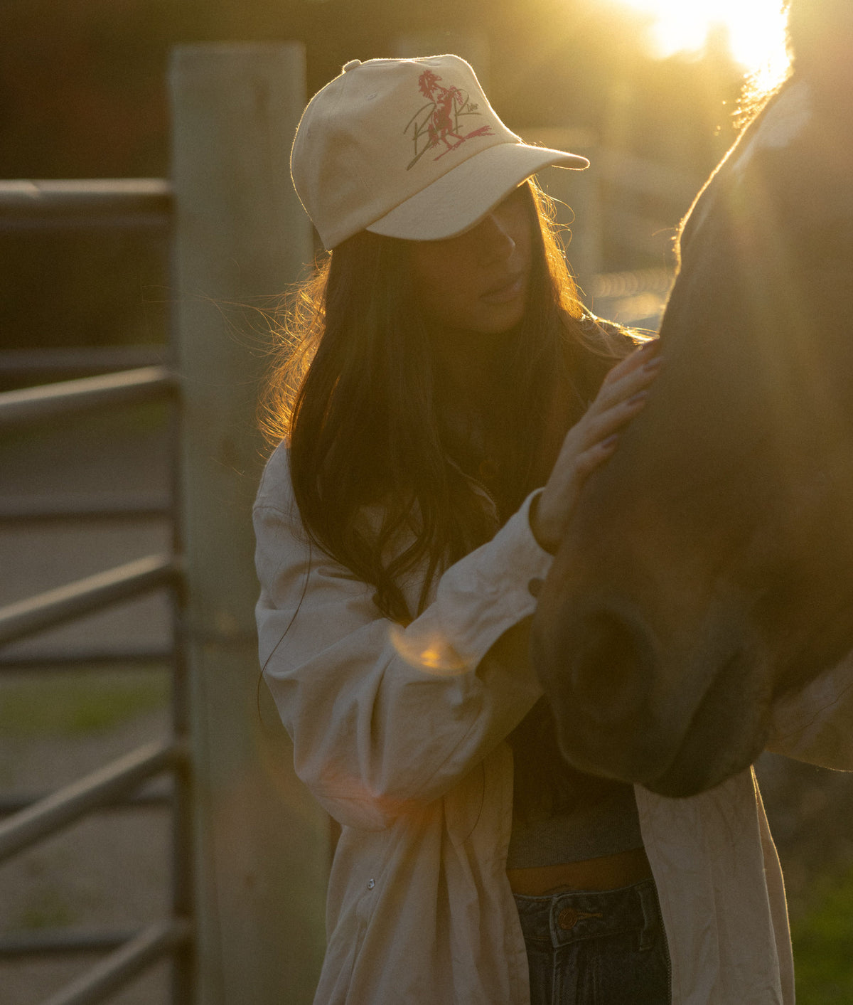 Woman in a tan Wild Card cap petting a horse