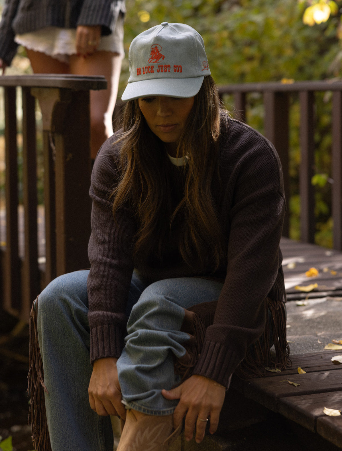 Woman seated wearing the No Luck light blue denim cap