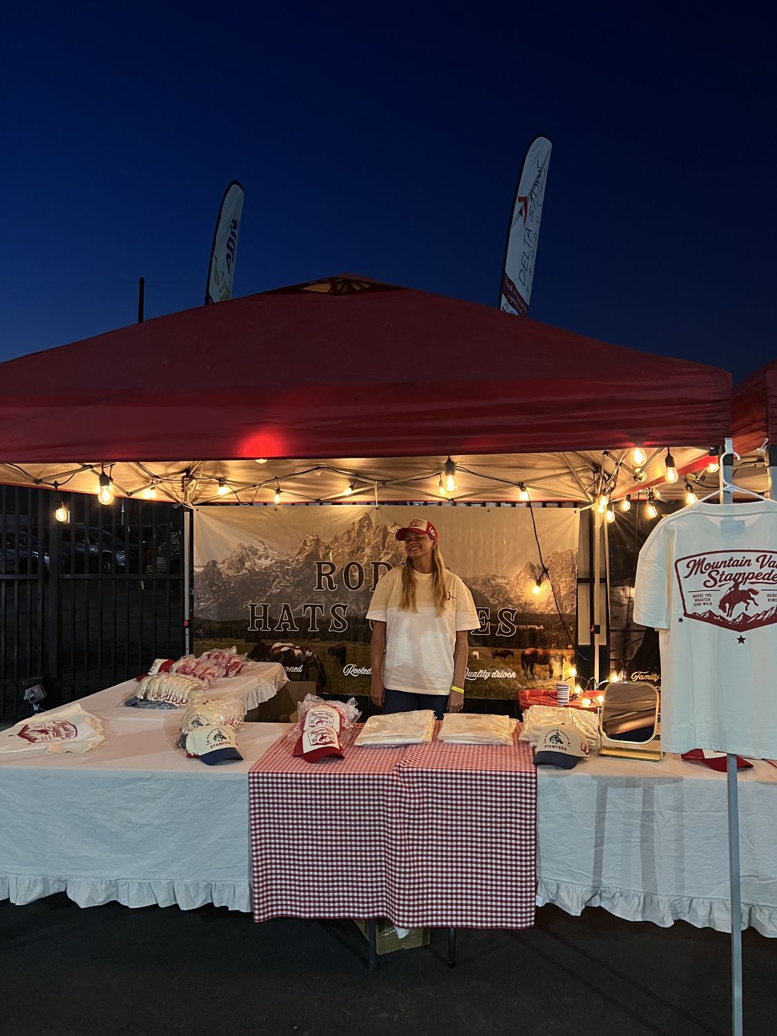 The Bull River booth lit up at blue hour with Mountain Valley Stampede hats and tees on the table