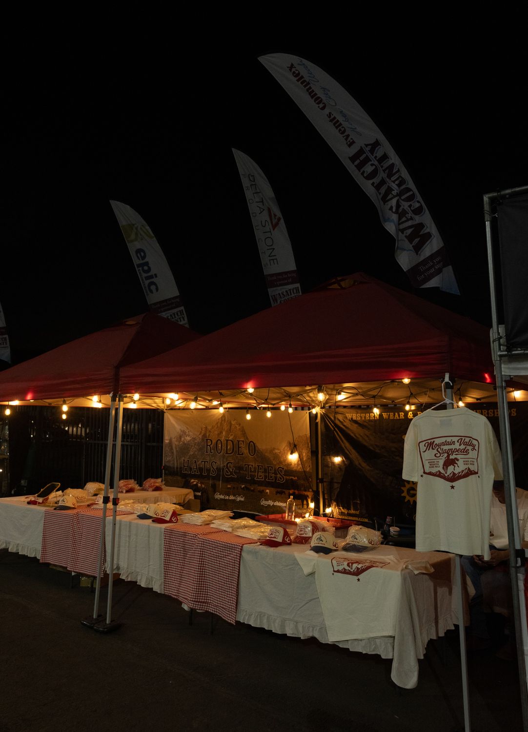 The Bull River tent lit up at night with hats and tees laid out for the rodeo crowd