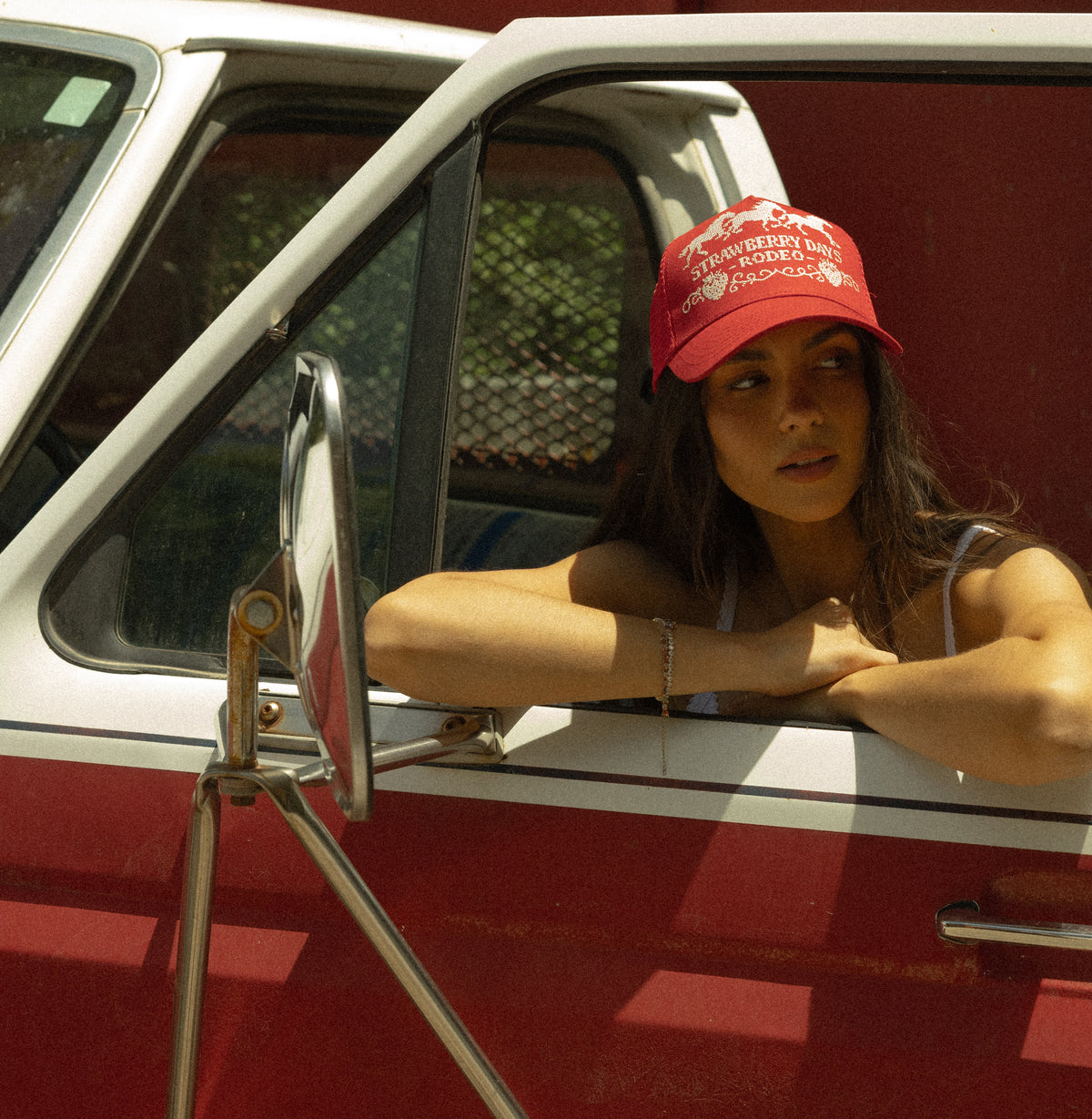 Woman leaning out of a red truck window in a Bull River rodeo hat