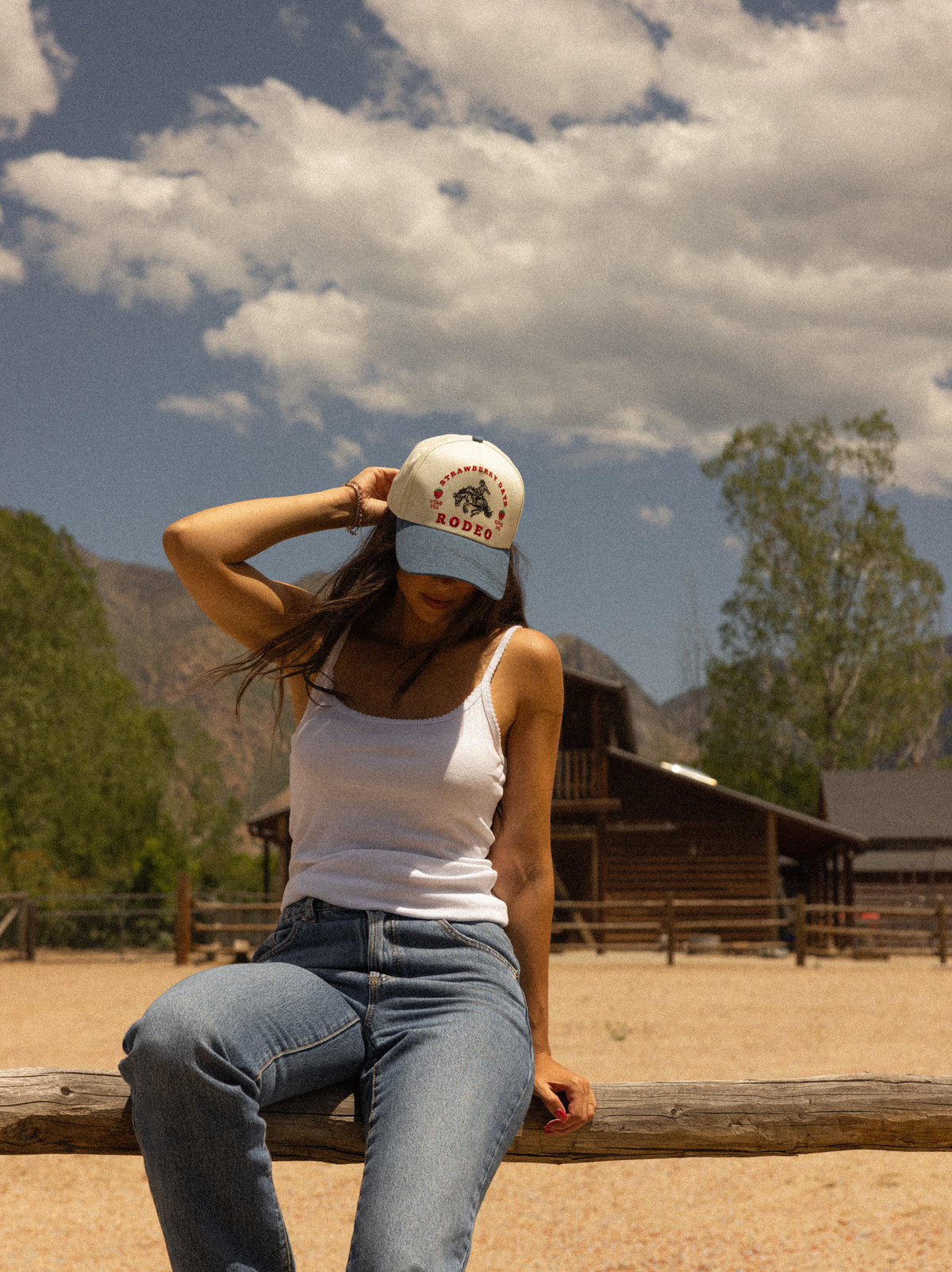 Woman seated outside a barn wearing a Bull River trucker hat